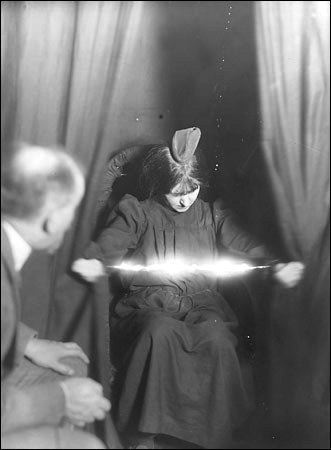 Eva C materilaising electricity from her body at a seance 1912